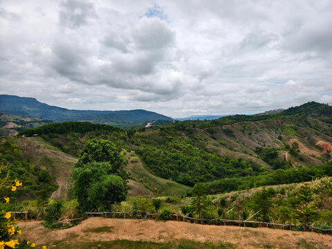 A beautiful panoramic view from a viewpoint overlooking lush green mountain ranges and hills under an overcast cloudy sky. Perfect for nature background and travel tourism concepts.