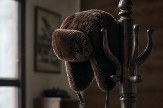Deep brown bearskin ushanka hat resting on a dark wooden coat rack.