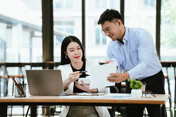 Obraz premium Smiling business colleagues collaborating at a modern office, reviewing work on a laptop while sharing ideas over coffee, highlighting teamwork, productivity, and professional communication.