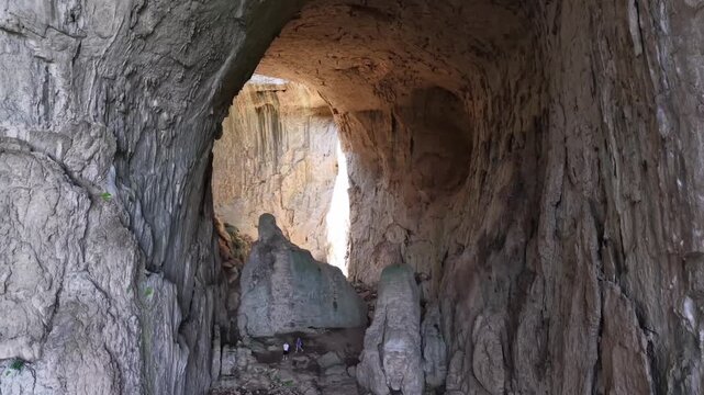 The cave walls feature a rugged, natural, and sturdy texture. In the center of the cave lies a large opening or natural passage that allows light to filter through, 