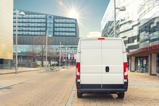 Small cargo delivery van driving in european city central district. Medium lorry minivan courier vehicle deliver package at residential office building in downtown area. Commercial shipping logistics
