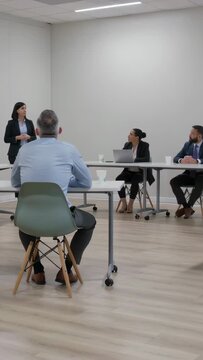 Vertical video: Starting presentation, woman in blazer speaking, gesturing in room with laptop
