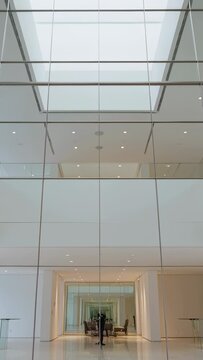 Vertical video: Tilting camera, man in dark clothes adjusting phone on tripod in atrium, recording