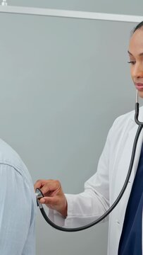 Vertical video: Doing clinic visit, doctor in coat placing steth on patient's back checking lungs