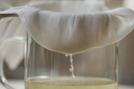 Fine cheesecloth straining liquid into a clear glass vessel, detail shot.