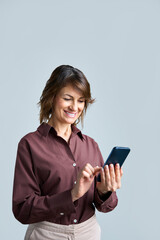 Fototapeta premium Mature latin smiling businesswoman using smartphone mobile device for online business office work standing isolated on light background. Middle-aged woman holding phone for communication, connection
