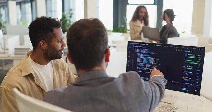 Programmer and developer teamwork coding software office. Teammates discuss source code on a computer screen and monitor in a bright office. Clear concept of teamwork and collaboration.