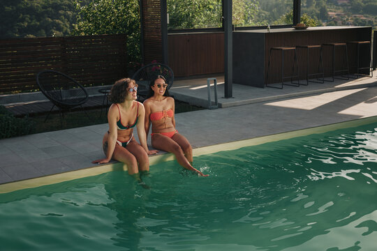 Women friends relaxing by swimming pool on summer vacation
