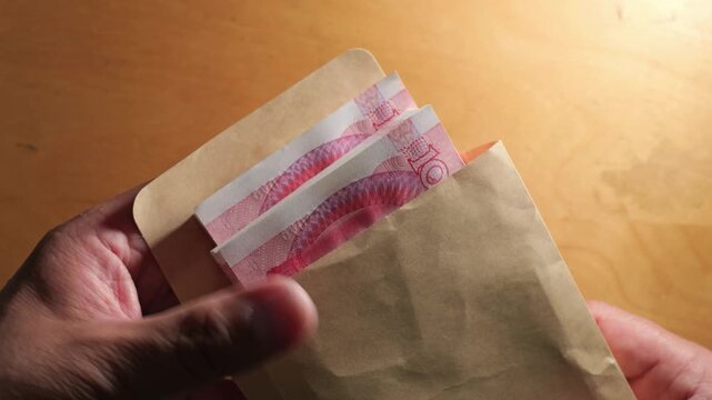 Hands putting Chinese Yuan banknotes inside a brown paper envelope during a cash transaction.