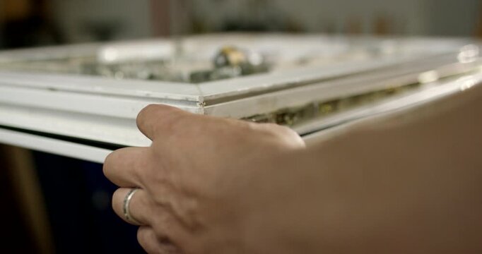 Close-up view of hands using a cordless electric screwdriver to install hardware on a white window profile