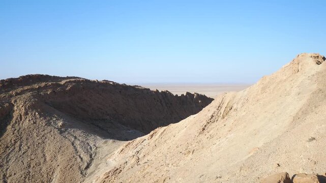PAN: Rugged phosphate-rich mountains rise from the arid landscape near Chebika, Tunisia, revealing layered rock formations, desert geology, and vast open terrain beneath a clear blue sky
