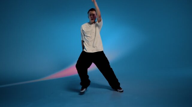 Hip hop dancer performing dynamic step in blue studio