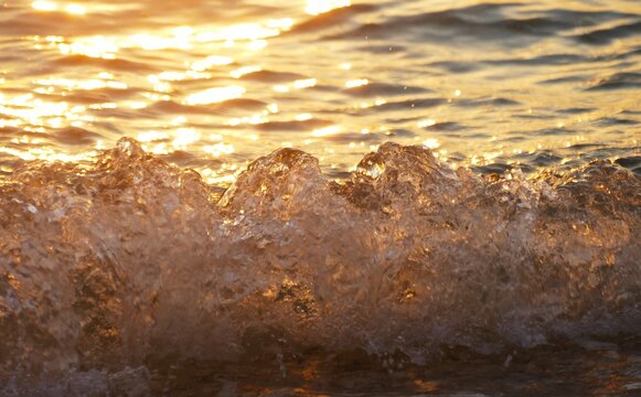 Golden wave sea splash on the beach in beautiful sunset with sparkle and shine,summer sea water splash background