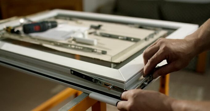 A person attaches long metal hardware tracks onto the outer edge of a white window sash frame