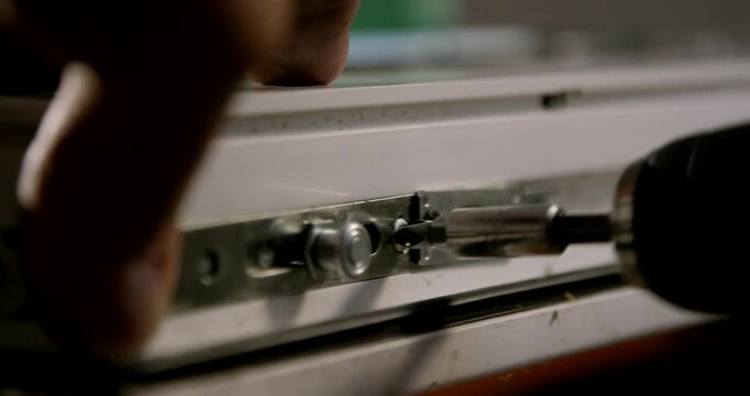 Macro shot of a cordless electric screwdriver fastening a screw into a metal window mechanism track