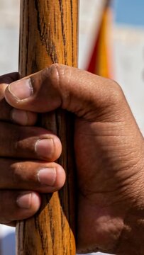 Vertical video: Gripping pole with right hand, man in white in parade while camera pulling, flags