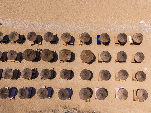 Aerial view of rows of straw umbrellas and sun loungers on a sandy beach in Sarande, Vlore County, Albania.