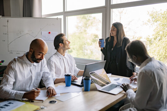 Team members, four diverse colleagues, engage in a brainstorming session in a bright office, sharing ideas and discussing projects while reviewing charts and graphs on a sunny afternoon