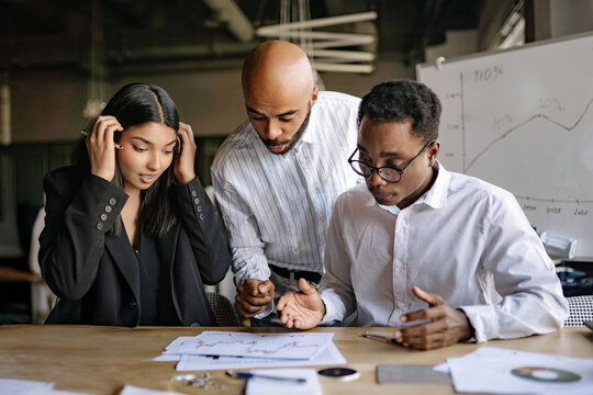 Diverse team, a group of three people, mentor and his colleagues, brainstorming session in a modern office while discussing complex financial charts and strategies on a busy afternoon