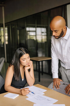 Two professionals, mixed race man and Indian woman, engage in a detailed conversation about investment education, analyzing documents and notes at a conference table in a contemporary office.
