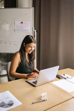 An Indian woman engages in focused office work at her desk, utilizing technology and surrounded by business documents in a contemporary workspace