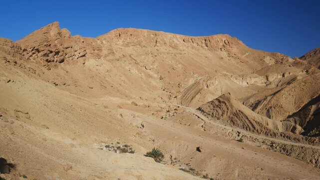PAN: Rugged phosphate-rich mountains rise from the arid landscape near Chebika, Tunisia, revealing layered rock formations, desert geology, and vast open terrain beneath a clear blue sky