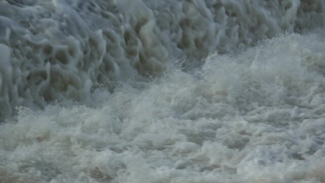 A wide perspective of a relentless wall of white water crashing at the base of a spillway, emphasizing scale and unyielding hydro energy.
