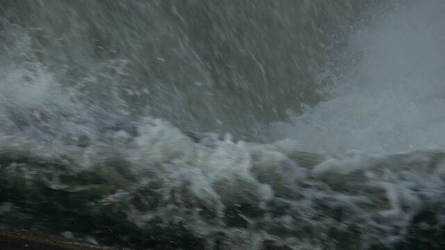 Dramatic slow motion close up of river water aggressively crashing and splashing over a rubber dam structure, showing immense natural force.
