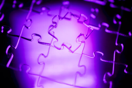 Close-up of interlocking puzzle pieces illuminated by purple light, showcasing intricate details and textures of the jigsaw puzzle against a blurred background