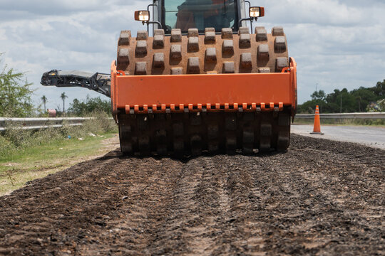 Front view of a heavy padfoot soil compactor roller flattening a dirt surface on a road construction site.