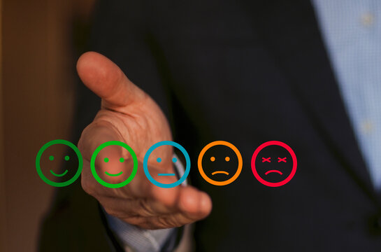 Businessman presenting five emoticons representing varying levels of satisfaction, hand extended forward, wearing a dark suit and light blue shirt in a professional setting