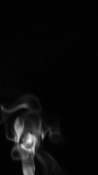 White natural steam or smoke rising from food or hot drink on black background. Vertical view.
