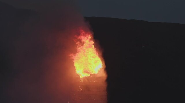 ALESUND, NORWAY, JUNE 20, 2026. Slinningsbalet burns brightly beside the sea in Alesund, Norway, a towering midsummer bonfire reflecting fiery light on dark water on a summer night