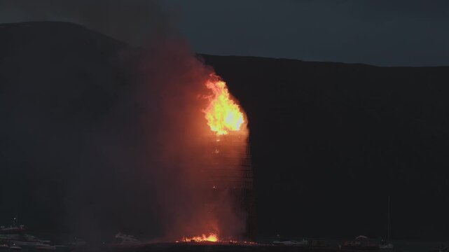 ALESUND, NORWAY, JUNE 20, 2026. Slinningsbalet burns brightly beside the sea in Alesund, Norway, a towering midsummer bonfire reflecting fiery light on dark water on a summer night