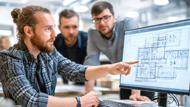 Professional architect collaboratively reviewing detailed floor plans and architectural blueprints on a large computer monitor with colleagues in a modern design studio.