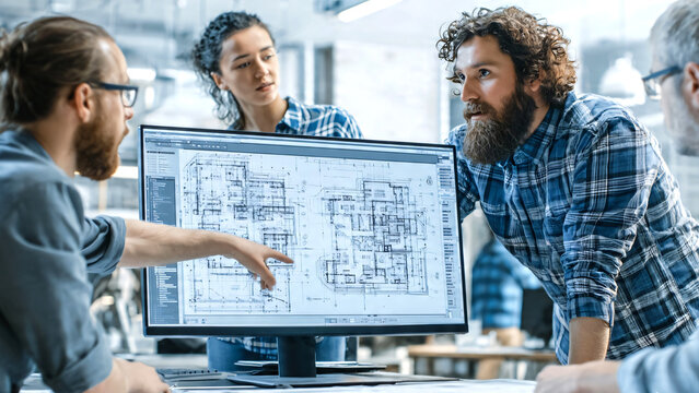Professional architect collaboratively reviewing detailed floor plans and architectural blueprints on a large computer monitor with colleagues in a modern design studio.