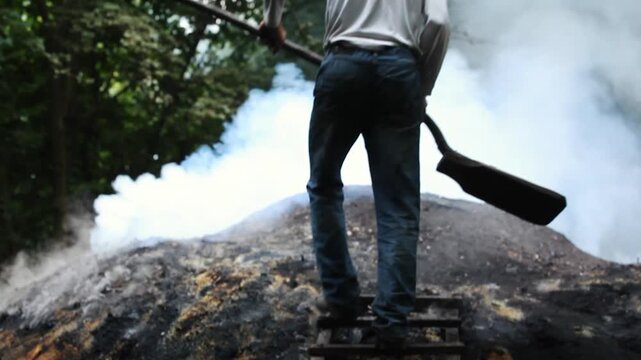 Traditional Charcoal Making: Worker Climbing a Smoking Kiln