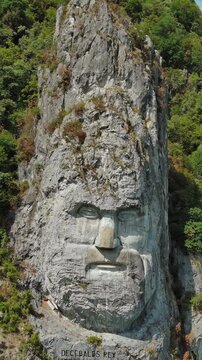 Aerial around view of stone carved statue portrait of ancient dacian king Decebal. Sculpture near Danube River, Romania. Vertical video 4k