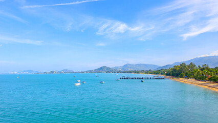 A breathtaking aerial view of a tropical bay with crystal-clear turquoise water, a sandy beach, and lush green hills in the distance. Several boats are anchored in the calm sea. ©  2026stockx