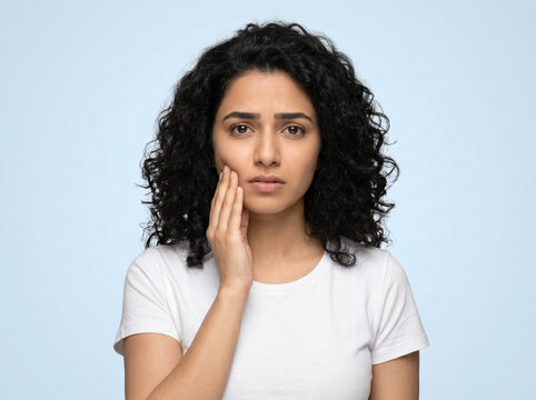 young indian woman touching cheek with sensitive teeth discomfort and oral healthcare awareness concept