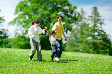 手を繋いで公園を歩く三人家族