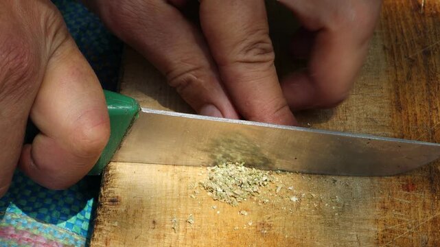 Marrakesh, Morocco - 20 June 2026: Hands chopping dried cannabis with a knife on a wooden board