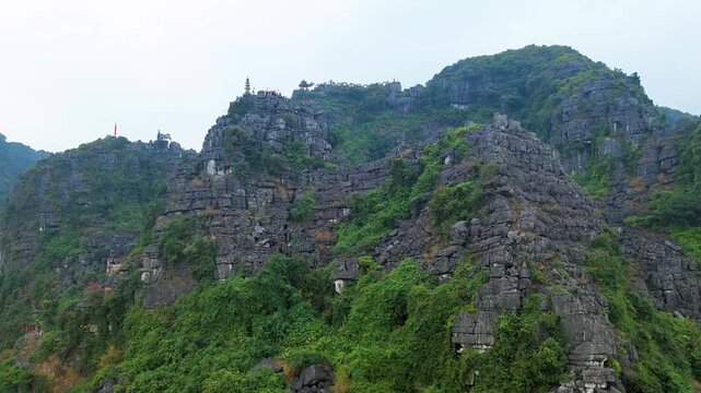 Aerial drone view of mountain temple stairs overlooking rice fields and limestone mountains in Tam Coc Vietnam
