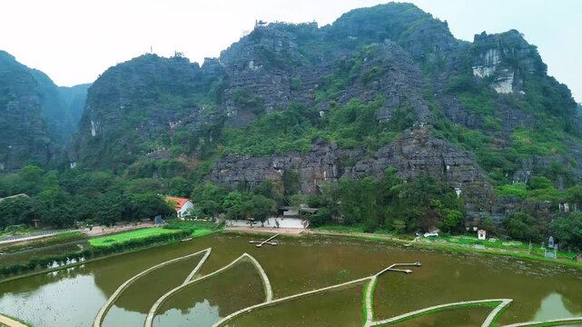 Aerial drone view of mountain temple stairs overlooking rice fields and limestone mountains in Tam Coc Vietnam