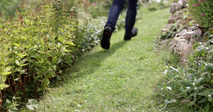 Close-up low angle shot of feet wearing black shoes and blue jeans running on green grass