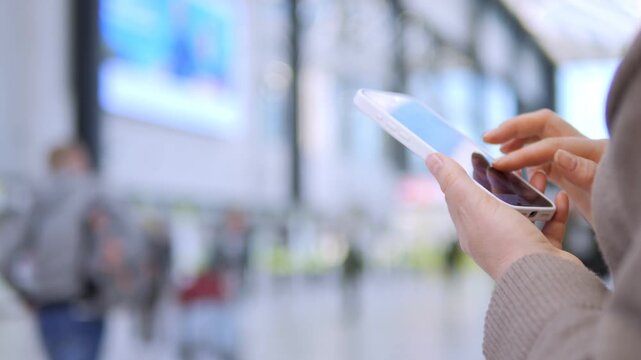 Hands hold tablet in busy transit area. Person focused, calm, navigating digital content. Background blurred, commuters move softly. Ideal for tech, travel, or urban connectivity themes