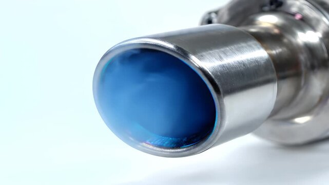 Close up of a metallic titanium exhaust pipe with a burnt blue tip emitting blue smoke against a white background