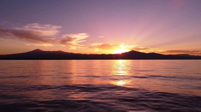 Sunset over a calm lake with silhouetted mountains and vibrant orange and purple sky reflecting on the water surface Keywords: sunset, lake, mountains, silhouette, water, sky, orange, purple