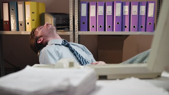 Exhausted office worker leaning back at cluttered desk