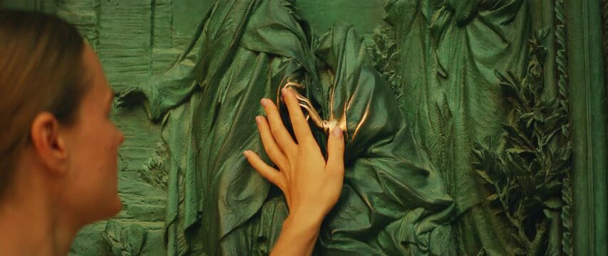 Close-up of a woman touching a polished bronze relief on a cathedral door